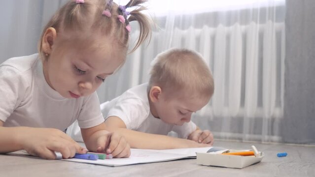 happy family brother and sister teamwork concept. little boy and girl draw on floor in a sketchbook. brother and sister in the room draw lifestyle with crayons