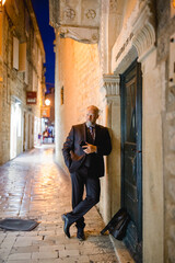eleganter Mann im Anzug lehnt lässig am Tor, abends in Altstadt-Gasse, Hochformat