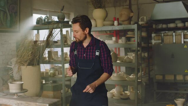 Young man potter is dancing alone in big studio, having fun, enjoying his creative space, full of positive and creative energy to start new working day, Slow motion.
