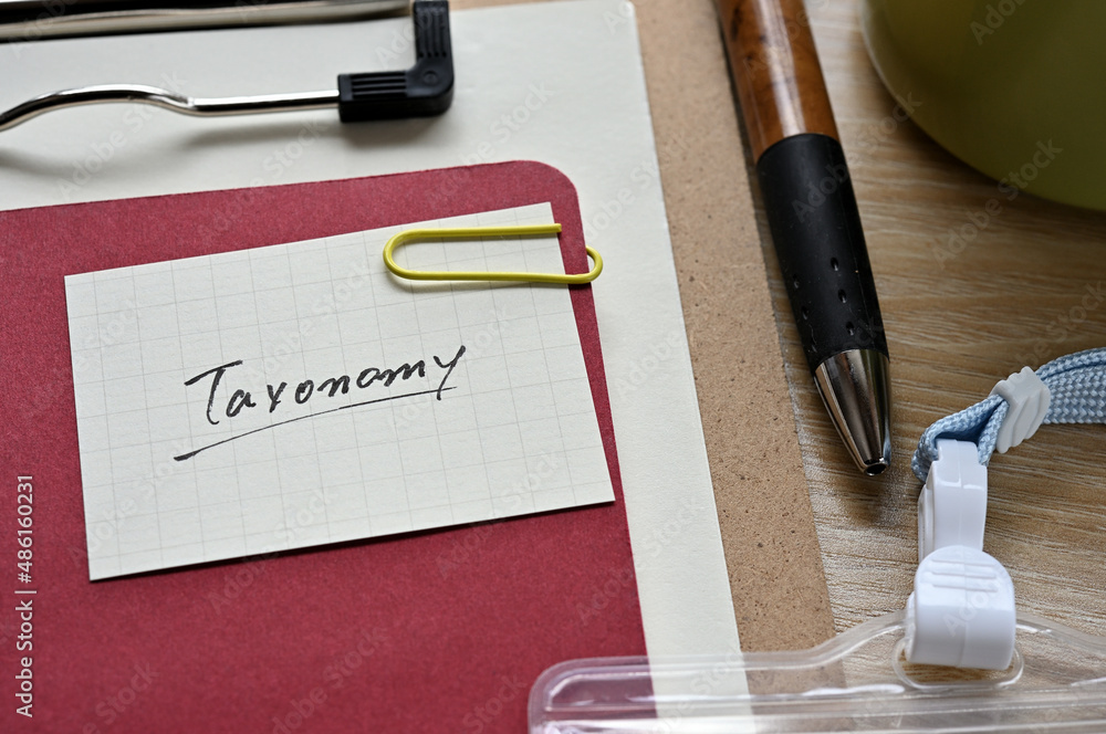 Poster a piece of paper clipped to the edge of the red notebook has taxonomy.