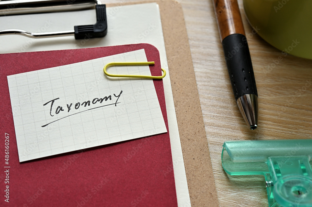 Poster a piece of paper clipped to the edge of the red notebook has taxonomy.