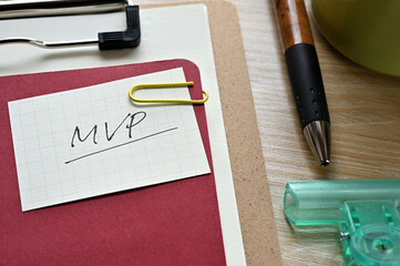 A piece of paper clipped to the edge of the red notebook has MVP written on it. It is an...
