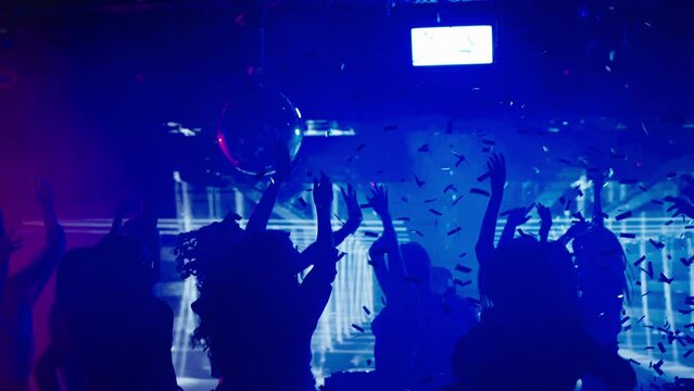 Cheerful people enjoying evening party in club. Dancing at disco with raised hands. Nightlife, modern music and entertainment concept.