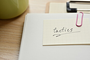 A piece of paper clipped to the edge of the notebook has Tactics.