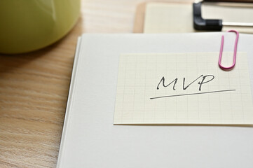 A piece of paper clipped to the edge of the notebook has MVP written on it. It is an abbreviation...