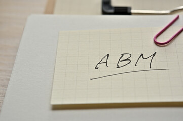 A piece of paper clipped to the edge of the notebook has ABM written on it. It is an abbreviation for Account Based Marketing.