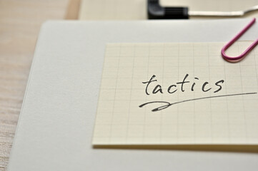 A piece of paper clipped to the edge of the notebook has Tactics.