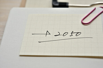 A piece of paper clipped to the edge of the notebook has 2050.