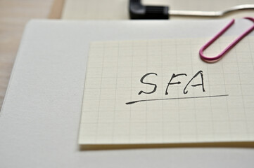 A piece of paper clipped to the edge of the notebook has SFA written on it. It is an abbreviation for Sales Force Automation.