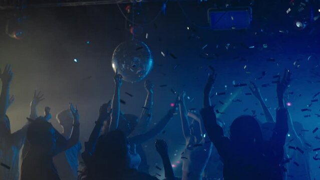 People dancing at disco, flashing light and falling confetti. Nightlife, modern music and entertainment concept.