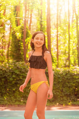 Girl in a swimsuit near the pool on a sunny day. Teenager 11 years old smiling.