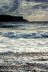 Naklejka na ściany i meble Powerful waves in the ocean. Cliffs in the background. Dramatic cloudy sky. Seascape scene. Doolin, county Clare, Ireland. Irish landscape and rugged nature. Dark and dramatic tone. Vertical image
