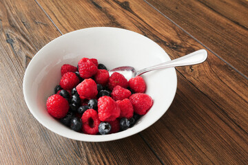 Raspberry and blueberry in a white bowl on a wooden table. Healthy fruit mix. Produce product. Healthy diet choice.