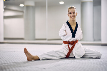 Happy female martial arts athlete with disability warming up while exercising taekwondo in health...