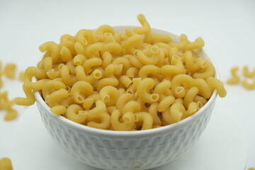 Raw macaroni in white bowl on white background