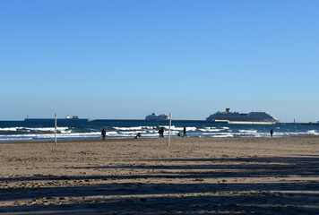People a walk on the beach near the sea during a pandemic. Cruise ship in port Valencia. Ship Tour on Cruise liner on mediterranean sea.  Travel on Cruise liner. View from coastline Las Arenas beach.