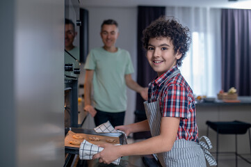 Boy taking pan out of oven looking at camera