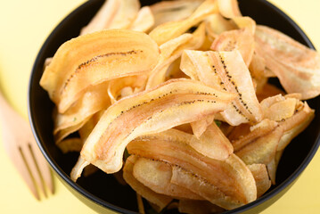 Banana chips or banana crisps in black bowl on yellow background, Delicious snack