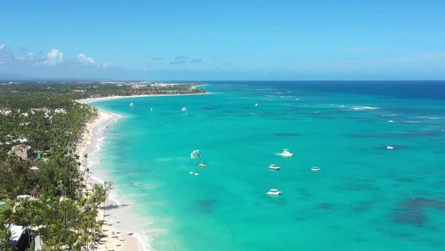 Tropical coastline with resorts, palm trees and caribbean sea with floating boats and people having fun doing paraseiling. Travel destinations. Dominican Republic. Aerial view