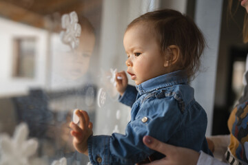 One small caucasian baby girl standing by the window at home looking outside waiting real people childhood and growing up concept