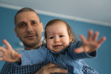 One frustrated baby trying to reach camera crying in hands of her father holding her while standing at home wearing blue shirt real people copy space