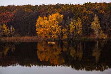 Yellow small boat near the forest with golden autumn trees