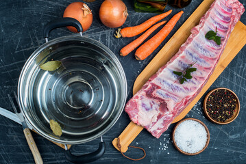 fresh meat and water in a saucepan on the kitchen table. Vegetables and spices for cooking broth