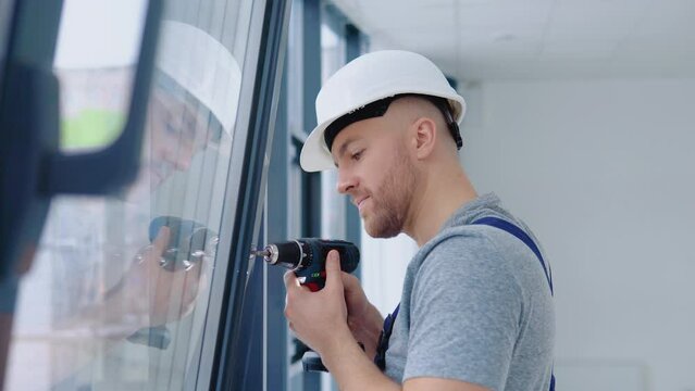 Window installer in a helmet and a screwdriver installs windows