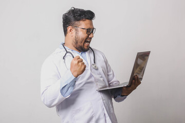 Male doctor holding laptop cheering cheerfully and excitedly