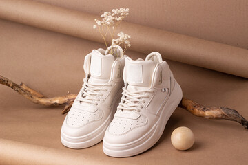 Eco leather shoes. A pair of beige sneakers with dry flowers on the wood, brown background. Casual sport lifestyle concept