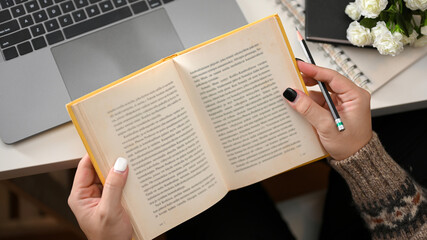 Female reading a novel book at her home office.