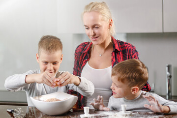 Young beautiful mother with two children preparing Breakfast. A young mother teaches her sons to cook. Photography represents family values, love and care.