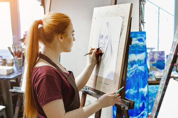 Young woman artist paints a picture in her studio