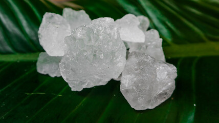 Crystal clear alum cubes or Potassium alum on green leaf. Chemical compound substance. Concept for beauty , spa and underarm treatment industrial. 