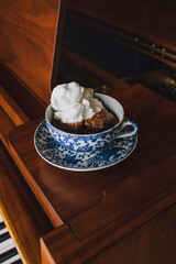 A hot drinking chocolate in blue floral teacup set with white meringue sitting on baby grand piano