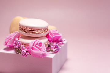 Macaroons with a decor in the form of pink flowers and a pink podium on a light red background.