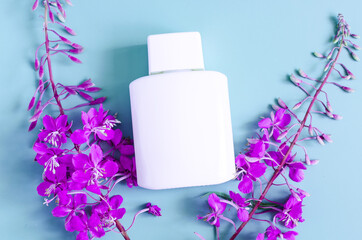 Lilac wildflowers and a bottle of white cosmetics on a blue background. Flowers and cosmetics on a light background a place for text.