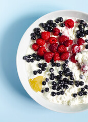 Light breakfast cottage cheese with sour cream and berries in a blue plate on a light background.