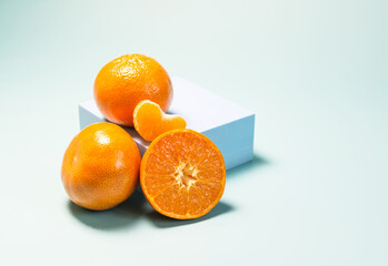 Tangerines and tangerine slices on a blue podium light blue background in natural light.