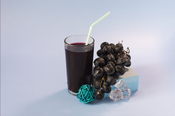 Grape juice and grapes. A vine and a glass of dark grape juice on a blue background close-up.