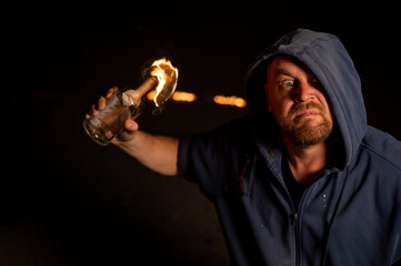 The man in the hood is holding a burning bottle. Molotov cocktail.