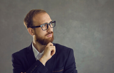 Portrait of thoughtful, creative and smart caucasian businessman or office manager in suit thinking planning project pondering idea dreaming in success looking aside standing on grey studio copy space