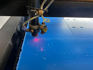 An electronic laser machine cuts plexiglass parts with a red laser beam.