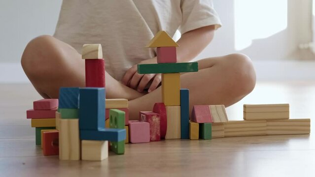Angry boy destroys what he built from colorful figurines standing on the floor in the playroom. Child development.