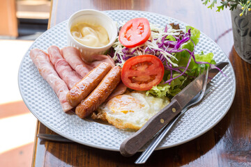 American breakfast with croissant, sandwich, jam, fried eggs, sausage, coffee, orange juice and salad on wood background.