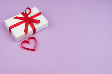 Valentine's Day or birthday concept with copy space. Red ribbon heart and gift box on purple papper