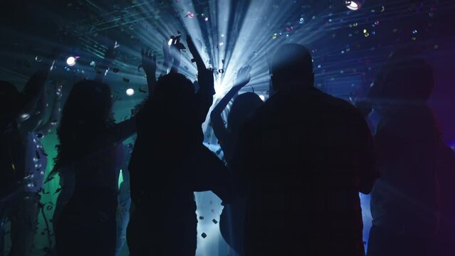 Back view of people dancing at disco. Falling confetti in bright flashing light. Nightlife, modern music and entertainment concept.
