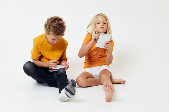 Boy and girl on the floor with notepads and pencils isolated background unaltered