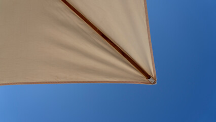 White beach umbrella. Blue sky in the background. View from below. Relaxing context. Summer holidays by the sea. General contest and location