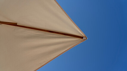 White beach umbrella. Blue sky in the background. View from below. Relaxing context. Summer holidays by the sea. General contest and location